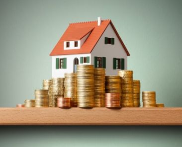 Miniature model house standing on a stack of coins.